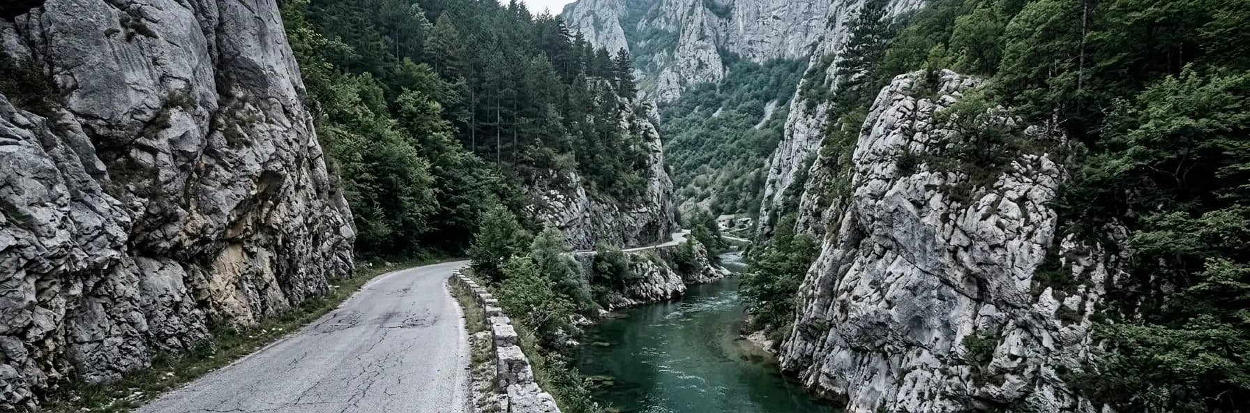 A narrow road following a green river through a steep limestone canyon in Bosnia and Herzegovina, dense forest on the slopes above.