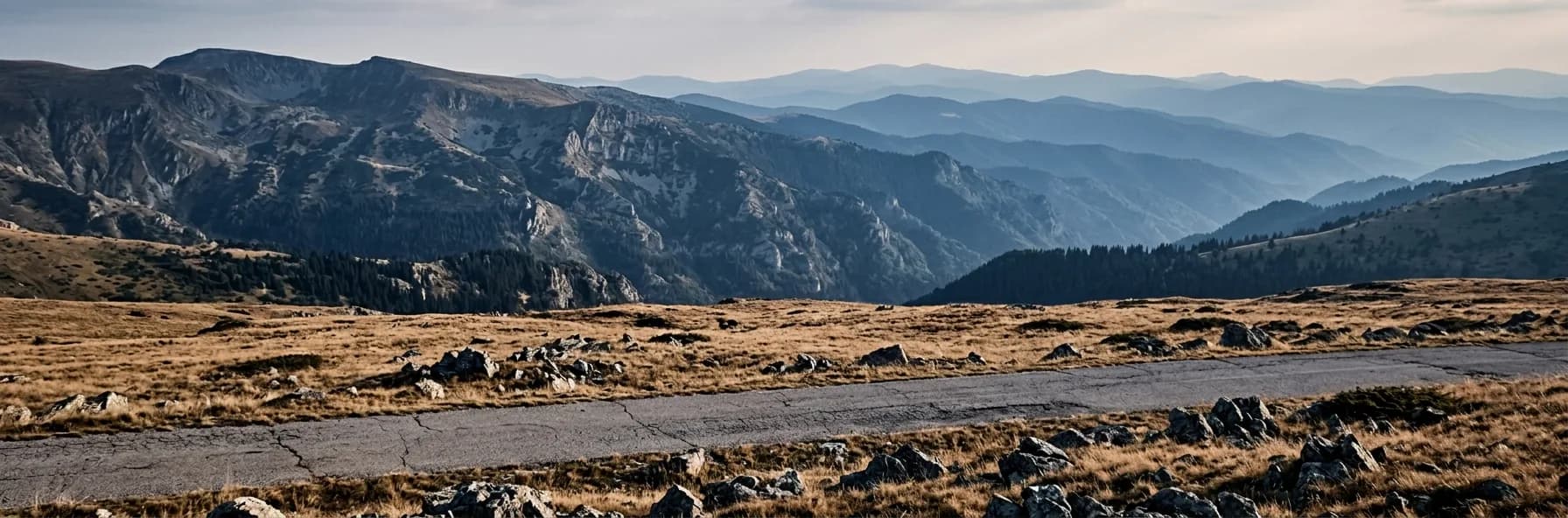 A road crossing high open pasture in the Balkan mountains of Bulgaria, with layered blue ridges receding to the horizon.