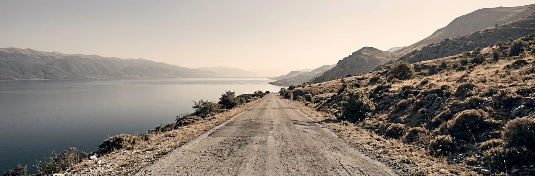 A road running above the shore of a large lake in North Macedonia, dry hills rising on one side and still water reaching to distant mountains.